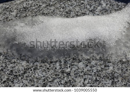 Close up outdoor view of snow and water on a marble plate. Picture taken in a french cemetery in winter just after a snowy day. Abstract urban image, with white, grey and black colors. 