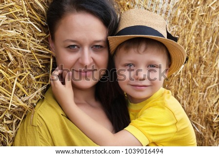 Happy family. A young woman with dark hair hugs her son in a hat against a background of hay. Mom and son.