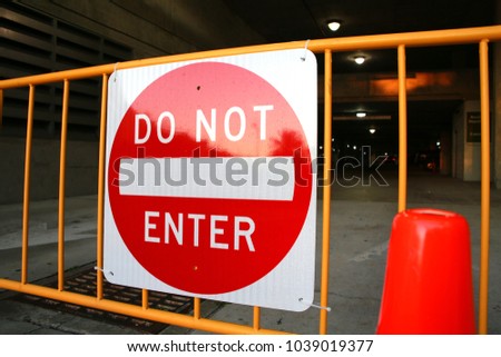 Do Not Enter Sign on Metal Railing Flanked by Two Cones in Front of Parking Garage at Dusk