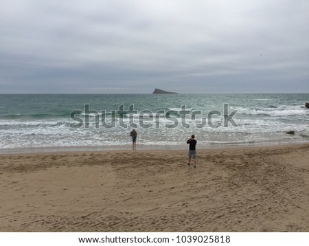 A young man takes a picture of his girlfriend at the beach of Benidorm-Spain.