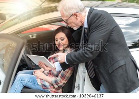 Car salesman giving explanations on tablet to pretty young woman, light effect