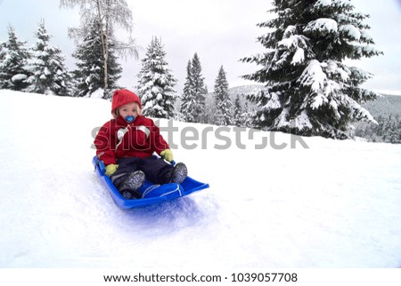 Child cute girl sitting on baby bob sled in winter forest
