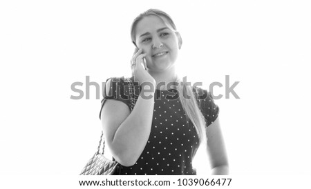 Monochrome portrait of young smiling woman talking by mobile phone