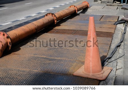 Orange funnel of traffic cone placed on metal sheet floor with drainpipe and road background, sign for beware driving, do not parking or under construction concept