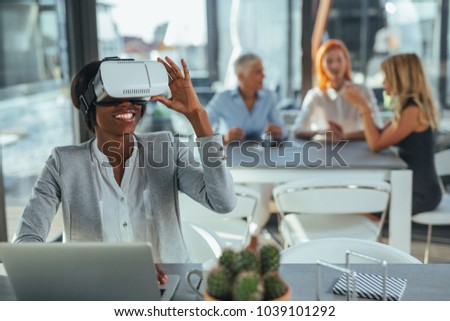 Young businesswoman holding a virtual reality headset , her colleagues sitting in the background