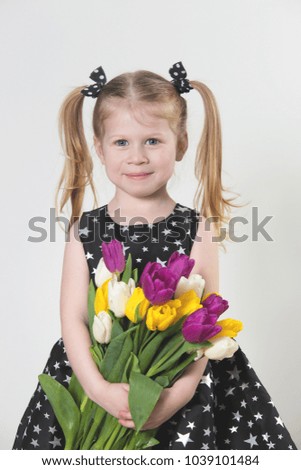 Happy blonde little girl with tulips. Caucasian smiling girl holding colorful tulips.