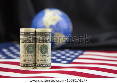 Focus on American currency placed on national flag with background in shallow depth of field.  Symbols of American policy, global trade, and national priorities placed against black satin background.
