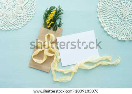 concept of International women's day mimosa brunch in Kraft envelope bag on a blue background, the bow of yellow silk with white blank card for text, crochet doily