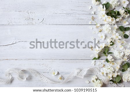 White wooden background with white spring flowers and lace ribbon