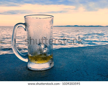 The empty of beer glass,the picture of a glass of beer beside the sea or lake while sunset.Concept of party or refreshness after work.