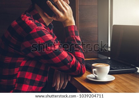 Young businessman enjoys coffee in the cafe talking on the phone and using a laptop