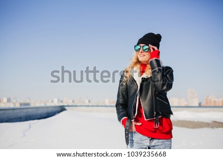 Fashion portrait of attractive stylish woman in sunglasses and cap enjoying outdoors in winter. Model looking at camera, wearing stylish winter clothes and enjoys sunny weather