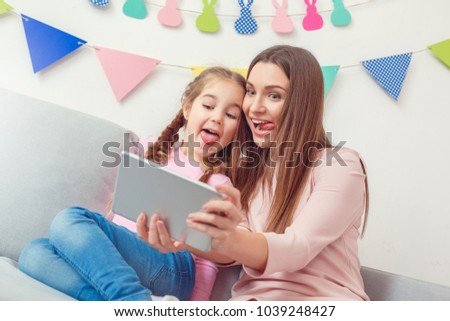Mother and daughter together weekend at home sitting holding digital tablet taking selfie pictures