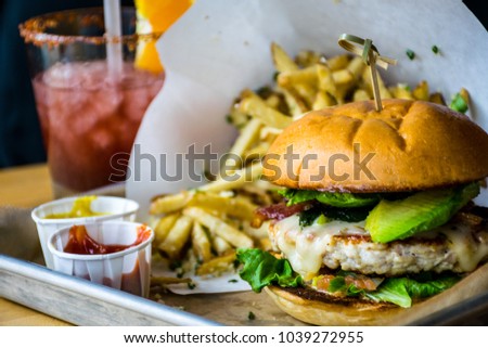Perfectly delicious Grilled chicken hamburger with bacon and avocado. truffle fries with ketchup and mustard. Red cocktail in the background and amazing delicious tasty food for lunch time