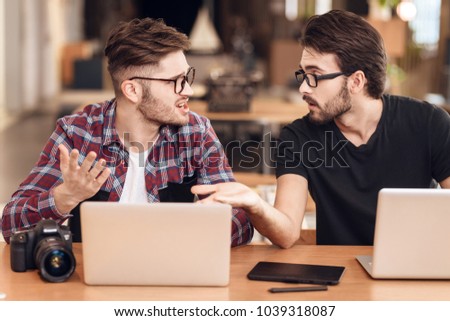 Two freelancer men in shirt and t-shirt discussing at laptop at desk.