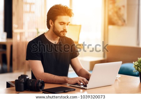 Freelancer bearded man in t-shirt typing at laptop sitting at desk.