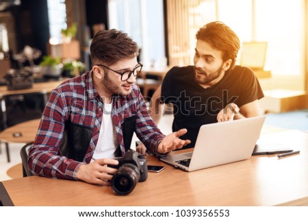 Two freelancer men in shirt and t-shirt looking at photos at laptop at desk.