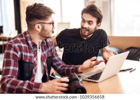Two freelancer men in shirt and t-shirt looking at photos at laptop at desk.