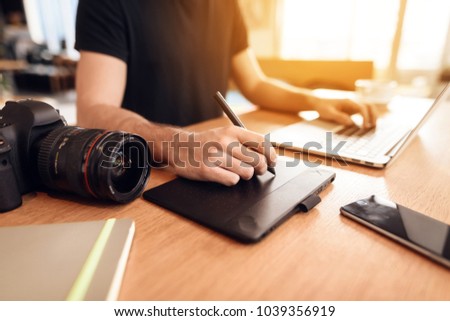 Close up freelancer bearded man wearing t-shirt drawing at laptop sitting at desk.