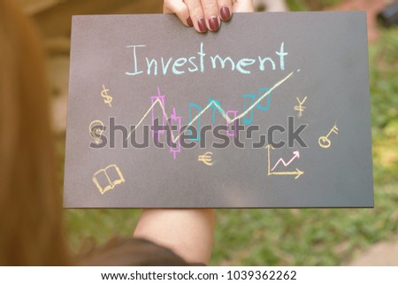 Woman holding a blackboard writing the word investment.