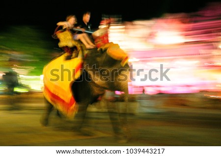 Tourist sit on elephan go around Phuket Fantasea Theater Hall at night. Take a photo by slow shutter and panning.