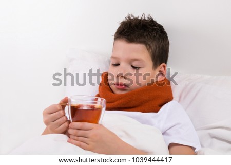 the boy drinks tea on the bed with a throat disease Royalty-Free Stock Photo #1039444417
