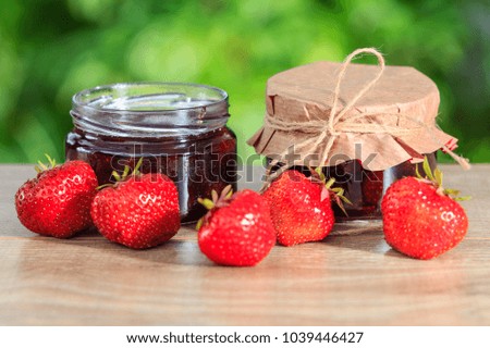 Traditional homemade strawberry jam in a jars, decorated with fresh strawberries on wooden table in green blurred natural background