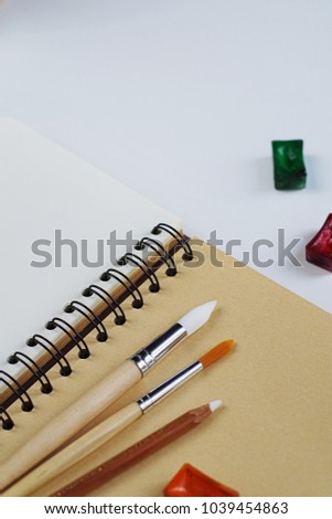 Blank paper with watercolor and brushes. Paints and blank notepad on white wooden desk, top view, copy space