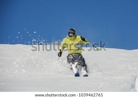 Skier dressed in yellow and grey sportswear running down the mountain slope and cutting up the snow in Gudauri, Georgia