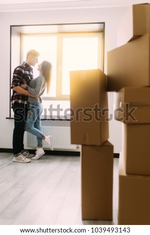 Portrait of beautiful young couple hugging and smiling while standing among moving cardboard boxes