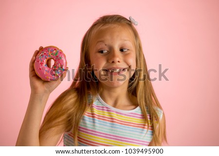 young beautiful happy and excited blond girl 8 or 9 years old holding donut on her hand looking spastic and cheerful in sugar calories and unhealthy sweet nutrition abuse addiction concept