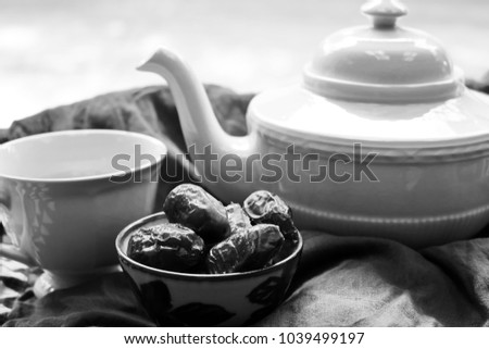 Black and white picture  set of tea in white cup and tea pot with bowl of dates fruit on cloth top table background, food for fasting in Ramadan, healthy food concept