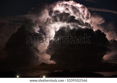 Close-up of dramatic thunderstorm with huge clouds and lightning over islands in the sea at night.