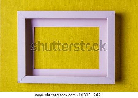Minimalism style. White empty picture frame against  abstract colored paper background, flat lay. 