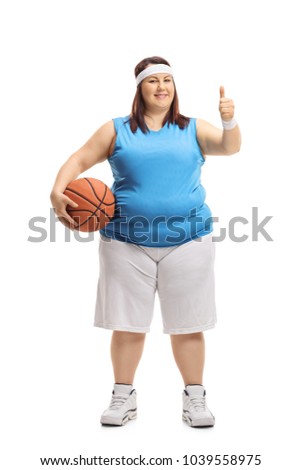 Full length portrait of an overweight woman in sportswear holding a basketball and making a thumb up sign isolated on white background