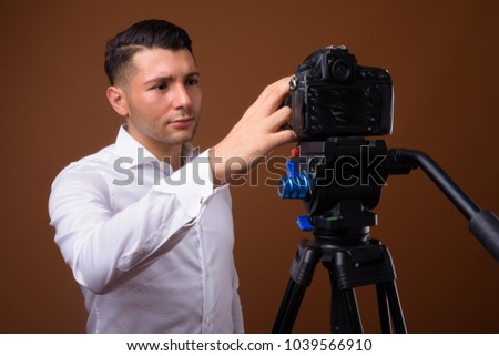 Studio shot of young handsome businessman vlogging against brown background