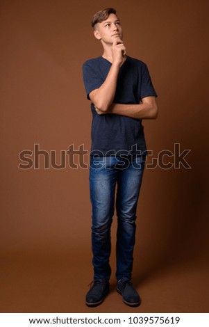 Studio shot of young handsome teenage boy wearing blue shirt against brown background