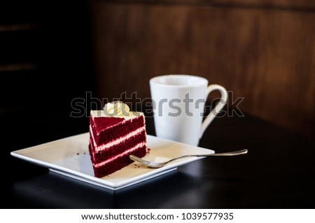 A cup of coffee served with a red velvet slice of cake 