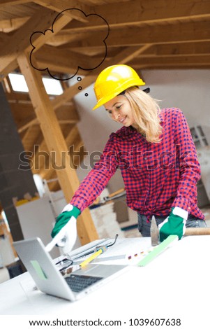 young, pretty, blonde woman with yellow helmet and green gloves is planning on the notebook and tablet the expansion of her loft