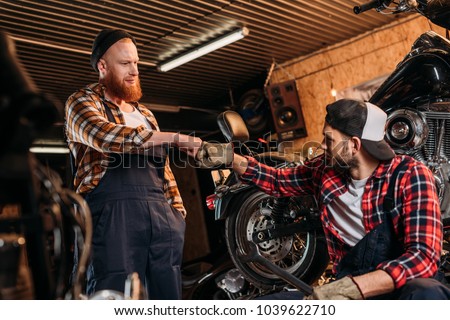 handsome mechanics making bro fist at motorcycle repair garage