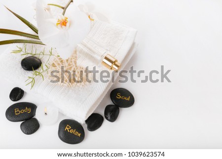 Spa resort therapy composition with burning candles, black stones, towel, and orchid on white 