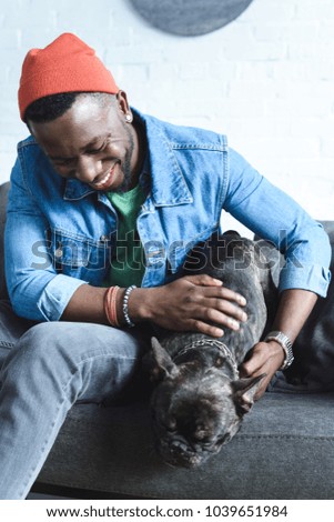 Handsome african american man playing with black Frenchie on sofa