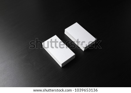 Two blank business cards stacks at black wood table background.