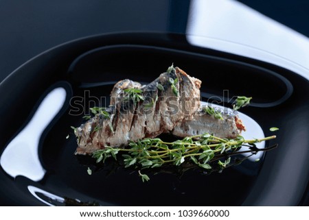 Grilled sardines with olive oil and thyme on a black plate.