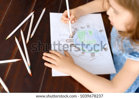 Portrait of cute little girl creating art on paper with colored pencils. The world through the eyes of a child expressed in the picture. As a child perceives the problem of ecology.