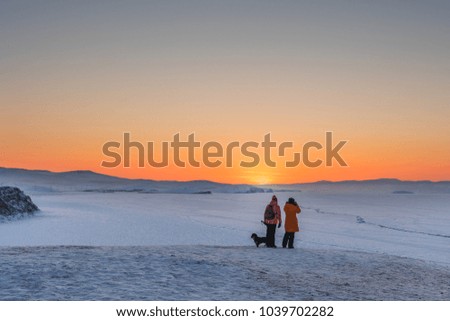 Couple with dog enjoying beautiful sunset view on sightseeing point at lake Baikal, Russia in winter