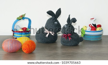 Easter decoration, two bunny rabbits made of gray socks, colorful decorative eggs with wrapped yarn, baskets, on wooden background. Shallow depth of focus. Homemade decoration, Easter concept. 