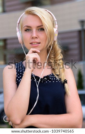 Woman with thoughtful face likes music. Woman with blonde hair enjoy sound with modern headphones. Young lady listening music headphones on urban background, defocused. Music and leisure concept.