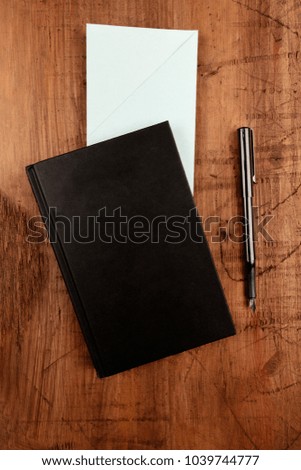An overhead photo of a black book, a blue envelope, and an ink pen, shot from above on a dark rustic background with a place for text