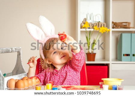 Easter day. Kid painting easter eggs in modern bright interior. Happy smiling child wearing bunny ears. Having fun on Easter egg hunt. Family preparing for Easter.